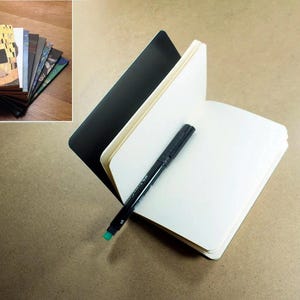 May include: A black notebook with a white interior and a black marker pen. The notebook is open and the marker is lying on the open pages.