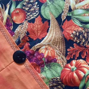 May include: A close-up of a fabric with a fall theme. The fabric features a cornucopia filled with pumpkins, corn, grapes, and fall leaves. The fabric is black with a variety of colors, including orange, red, green, and brown.