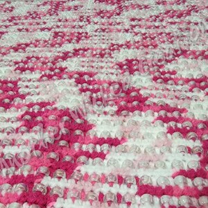 May include: A pink and white crocheted blanket with clear plastic beads woven throughout. The blanket has a diamond pattern.