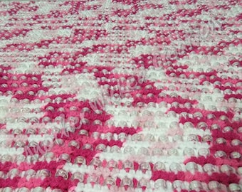 May include: A pink and white crocheted blanket with clear plastic beads woven throughout. The blanket has a diamond pattern.