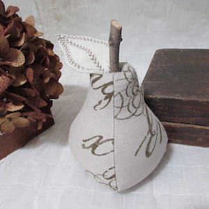 May include: A white pear-shaped pillow with a brown twig stem and a white fabric leaf. The pillow is decorated with a brown and gold swirl pattern.