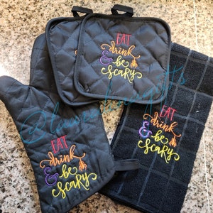 Puede incluir: Conjunto de tres textiles de cocina negros con el texto "Eat, drink & be scary" bordado en colores arcoíris. El conjunto incluye un posavasos, un guante para horno y un paño de cocina.