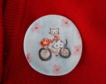 Handbemalte Keramikbrosche mit Katze auf einem Fahrrad, Blumenkatzenbrosche