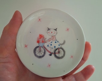 Lindo plato de anillo pintado a mano con gato montando en bicicleta, plato de anillo de gato colorido