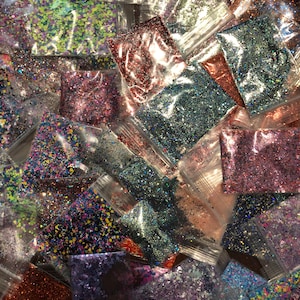 Op de afbeelding: Assortiment van kleine plastic zakjes gevuld met verschillende kleuren glitter. De glitter is in verschillende vormen en maten.