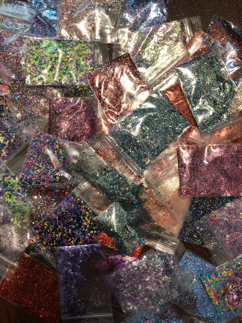 May include: Assortment of small plastic bags filled with various colors of glitter. The glitter is in a variety of shapes and sizes.