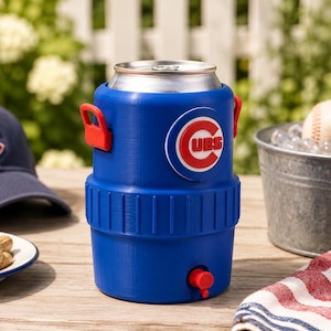 Może przedstawiać: Niebieska plastikowa chłodziarka do napoj&oacute;w zaprojektowana na standardową aluminiową puszkę, z czerwonym kranikiem u podstawy i okrągłym logo Chicago Cubs z przodu. Chłodziarka posiada dwa czerwone uchwyty boczne oraz żebrowaną środkową część.