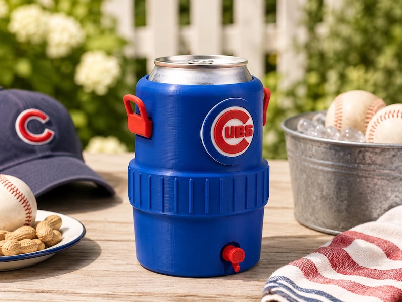 Może przedstawiać: Niebieska plastikowa chłodziarka do napoj&oacute;w zaprojektowana na standardową aluminiową puszkę, z czerwonym kranikiem u podstawy i okrągłym logo Chicago Cubs z przodu. Chłodziarka posiada dwa czerwone uchwyty boczne oraz żebrowaną środkową część.