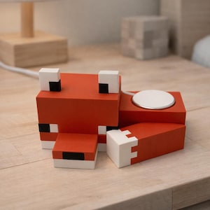 May include: A red and white fox-shaped charging station for a wireless charger. The fox is constructed from rectangular blocks with black accents. The charger is on a wooden surface.