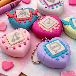 May include: A collection of heart-shaped toys in various colors, including pink, blue, and purple, with small screens displaying pixelated images. The toys are surrounded by heart-shaped erasers and crayons, creating a playful and colorful scene.