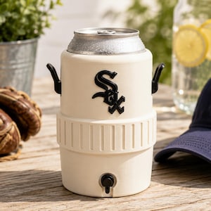 Może przedstawiać: Kremowy chłodziarka do napoj&oacute;w w kształcie miniaturowego kanistra na wodę z czarnym logo Chicago White Sox z przodu. Chłodziarka posiada mały czarny kranik u podstawy, dwa czarne uchwyty boczne oraz włożoną od g&oacute;ry srebrną metalową puszkę z napojem.