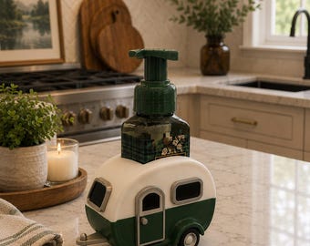 May include: A novelty soap dispenser in the shape of a retro caravan. The caravan is white and dark green with black details. The soap dispenser has a green pump and is placed on a marble countertop.