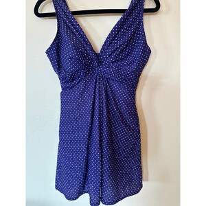 May include: A sleeveless dress in a deep purple hue featuring a white polka dot pattern. The garment has a V-neckline with a central twisted knot detail at the bust, leading into a gathered, flowing skirt that falls to a short length.