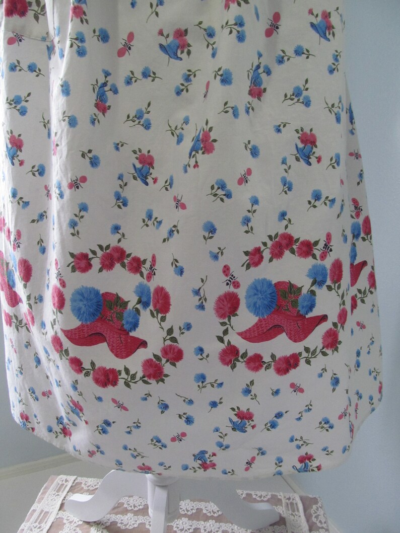 May include: White cotton fabric with a repeating pattern of pink flowers and blue birds. The fabric has a scalloped edge.