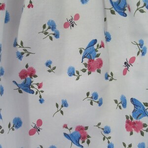 May include: White fabric with a repeating pattern of blue flowers, pink flowers, and blue butterflies. There are also small pink bees scattered throughout the pattern.