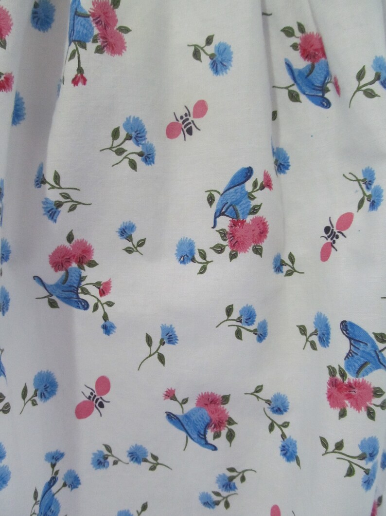 May include: White fabric with a repeating pattern of blue flowers, pink flowers, and blue butterflies. There are also small pink bees scattered throughout the pattern.