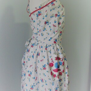 May include: A white dress with a blue and pink floral print. The dress has a halter neckline and a red trim around the neckline. The dress has a single pocket on the right side.