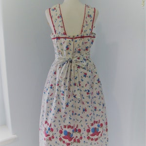 May include: A white sleeveless dress with a floral print featuring red, blue, and white flowers. The dress has a red trim around the neckline and a bow at the back.