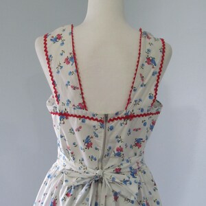 May include: A white dress with a blue and pink floral print. The dress has a red trim around the neckline and a bow at the back.