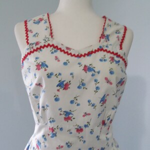 May include: A white sleeveless dress with a red trim around the neckline and armholes. The dress has a floral pattern with blue and pink flowers.