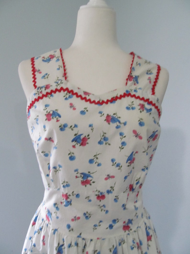 May include: A white sleeveless dress with a red trim around the neckline and armholes. The dress has a floral pattern with blue and pink flowers.