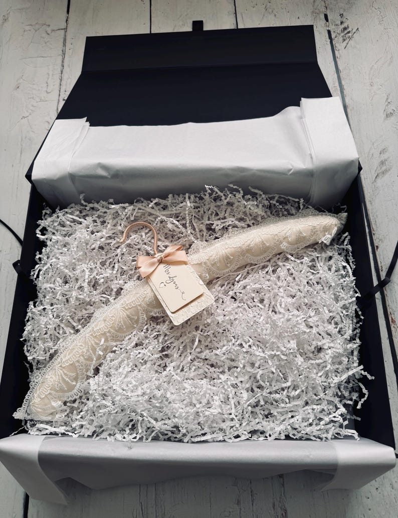Op de afbeelding: Een gevoerde kledinghanger bekleed met cr&egrave;mekleurig kant, voorzien van een ros&eacute;gouden haak en een klein rechthoekig label vastgemaakt met een perzikkleurig lint. Op het label staat de handgeschreven tekst Mrs Lyons met een hartje eronder.
