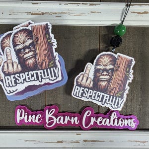 May include: Air fresheners featuring a Bigfoot graphic giving the middle finger, with the text "RESPECTFULLY". The air fresheners are displayed in a white distressed frame, with a green and black bead hanging.