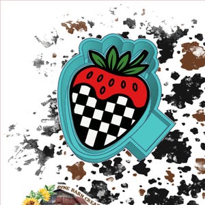May include: A turquoise strawberry-shaped cookie cutter with a checkered pattern on the bottom half and a red top with green leaves. The cutter has a handle on the side. The image has a white background with black and brown splatters.