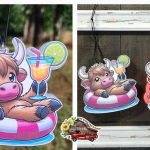 May include: A brown and white Highland cow cartoon character wearing a pink and white inner tube and holding a glass of orange juice with a lime wedge and a straw. The character is floating in blue water. The image is a car air freshener.