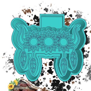 Könnte beinhalten: Türkisfarbener Metall-Ausstecher in Form eines dekorativen Designs. Das Design zeigt drei Sonnenblumen, Federn und eine rechteckige Oberseite. Die Worte "PINE BARN CREATIONS" stehen unten.