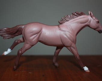 Puede incluir: Una figurita de caballo marrón y blanco con una melena y cola fluidas. El caballo está en una pose de carrera con las piernas extendidas.