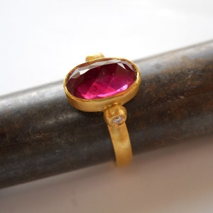 May include: A gold ring with a pink oval gemstone and two small white gemstones.