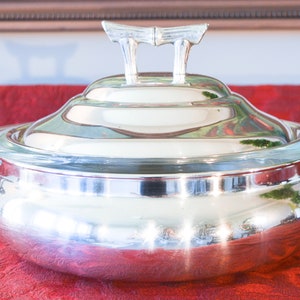 May include: A silver serving dish with a glass lid and a decorative bamboo handle. The dish is round and has a fluted edge. The lid is clear and has a slightly domed shape.