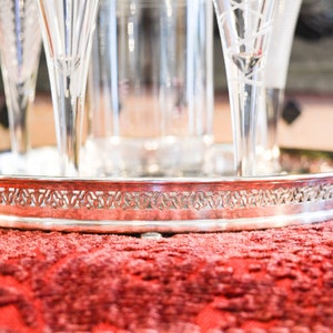 May include: A silver serving tray with a decorative border and a set of four clear glass champagne flutes.