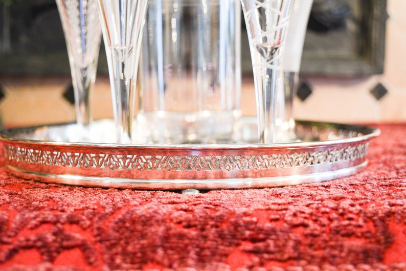 May include: A silver serving tray with a decorative border and a set of four clear glass champagne flutes.