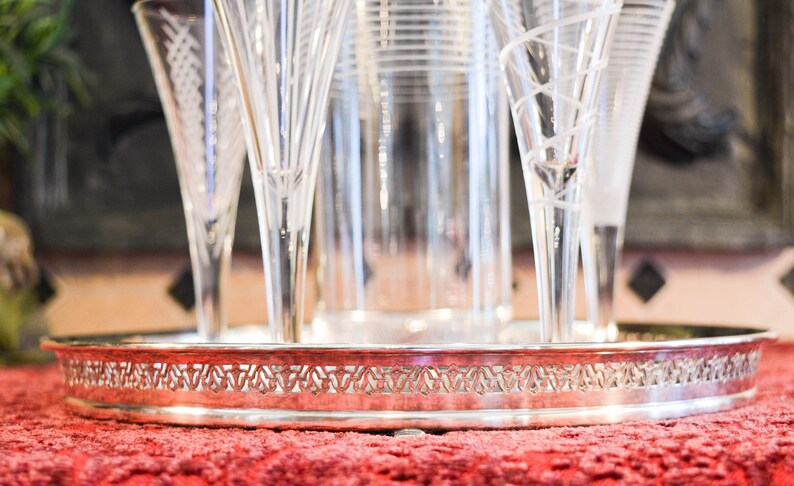 May include: A silver serving tray with a decorative border, holding a set of six clear glass champagne flutes.
