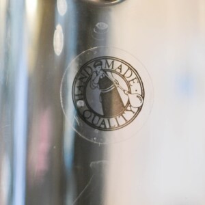May include: A clear glass bottle with a black and white sticker that says "Handmade Quality" and features a woman blowing glass.