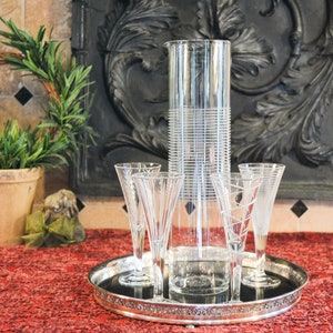 May include: A silver tray with four clear glass champagne flutes and a tall, clear glass pitcher with a textured design.