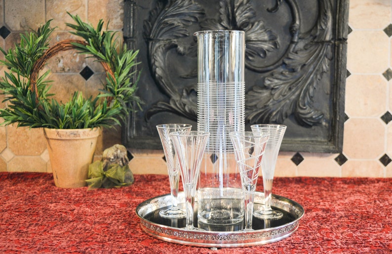 May include: A silver tray with four clear glass champagne flutes and a tall, clear glass pitcher with a textured design.