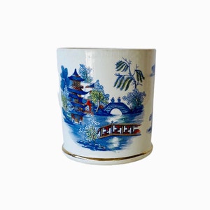 May include: A white ceramic mug with a blue and white design of a pagoda, bridge, and trees. The mug has a gold rim.
