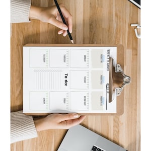 May include: A wooden clipboard with a weekly planner, a pencil, and a laptop on a wooden surface. The planner includes sections for each day of the week, a to-do list, and priority sections. The text "WEEKLY PLANNER" is visible.