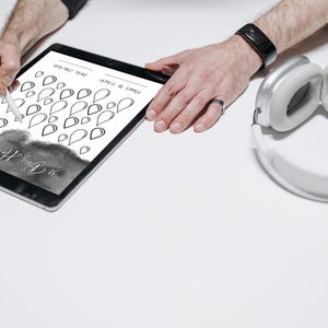 May include: A black tablet with a teardrop design being drawn on with a stylus. White headphones are placed next to the tablet. The tablet's text reads "24 Days After That".
