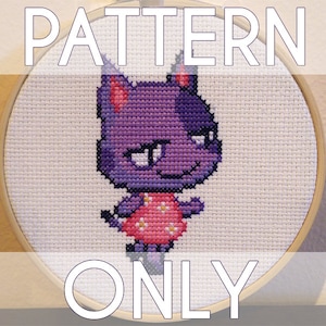 Puede incluir: Patrón de punto de cruz de un gato morado con un vestido rosa con flores blancas. El patrón está en un aro de bordado de madera redondo. El texto "PATTERN ONLY" está arriba y abajo de la imagen.