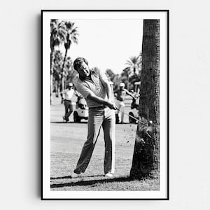 Puede incluir: Impresión enmarcada en blanco y negro de un golfista en pleno swing, golpeando una pelota cerca de un árbol. El golfista lleva una camisa con cuello y pantalones. Se ven carritos de golf y otros golfistas en el fondo.
