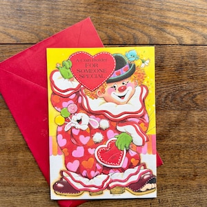 May include: A vintage clown-themed greeting card with the text "A Coin Holder For Someone Special." The card features a colorful clown illustration with a heart-shaped coin holder. A red envelope is visible.