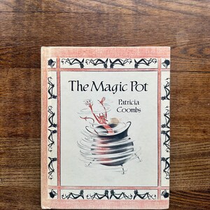 May include: A vintage book cover with a pink background and a black border. The title "The Magic Pot" is written in black text. The author's name, "Patricia Coombs", is written in smaller black text below the title. An illustration of a red devil in a black pot is shown in the center of the cover.