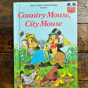 May include: A vintage children's book cover featuring a cartoon illustration of a country mouse and a city mouse. The book title is "Country Mouse, City Mouse" and is presented by Walt Disney Productions. The cover is blue with a white border and features a cartoon illustration of a country mouse and a city mouse.