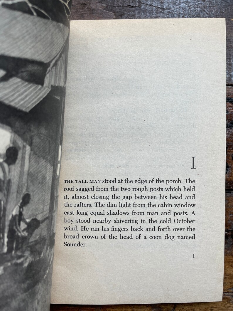 May include: A black and white photo of a book with the text "THE TALL MAN stood at the edge of the porch. The roof sagged from the two rough posts which held it, almost closing the gap between his head and the rafters. The dim light from the cabin window cast long equal shadows from man and posts. A boy stood nearby shivering in the cold October wind. He ran his fingers back and forth over the broad crown of the head of a coon dog named Sounder."