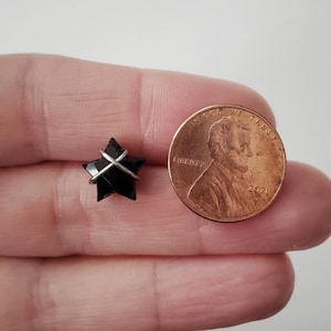 Puede incluir: Una piedra preciosa negra en forma de estrella envuelta en alambre plateado. La estrella es aproximadamente del tama&ntilde;o de una moneda de un centavo de euro.