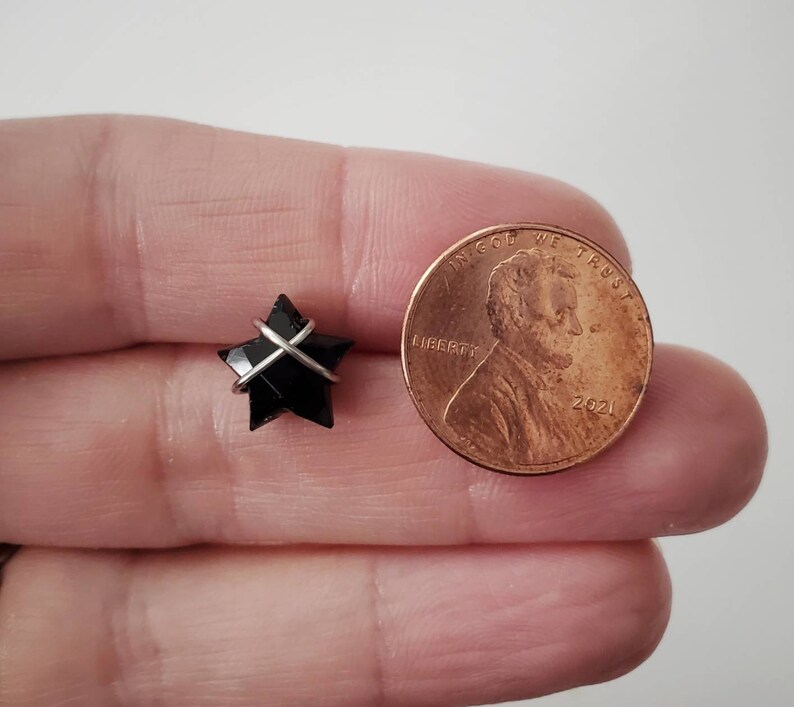 Puede incluir: Una piedra preciosa negra en forma de estrella envuelta en alambre plateado. La estrella es aproximadamente del tama&ntilde;o de una moneda de un centavo de euro.
